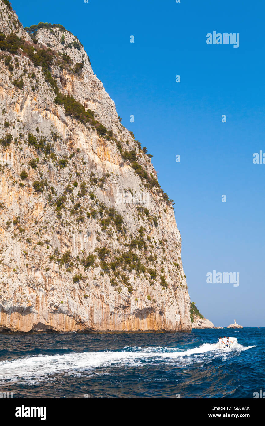 Piccolo piacere motoscafo con i normali turisti andare vicino a rocce costiere di isola di Capri, Italia Foto Stock