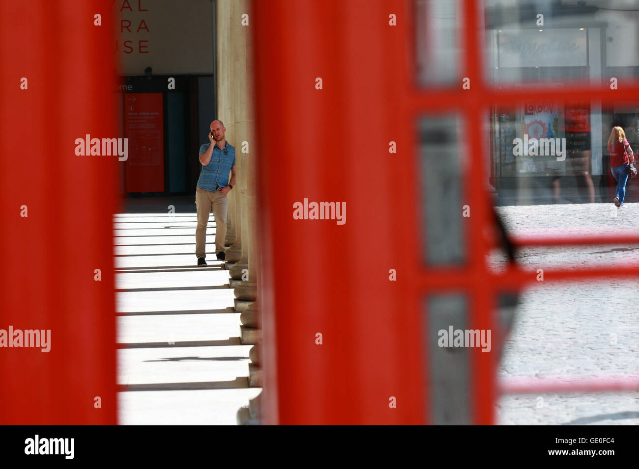 Un maschio utilizzando il suo telefono cellulare in Covent Garden di Londra, Inghilterra. Visto attraverso un interstizio tra due telefono rosso chioschi. Foto Stock