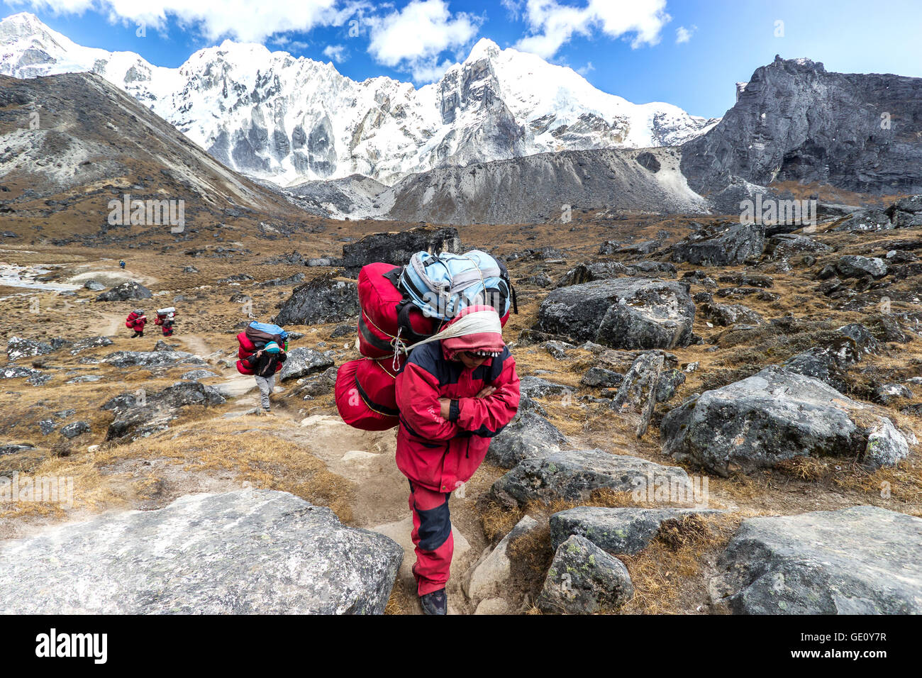Facchini con carico pesante dopo aver attraversato Cho La Pass in Himalaya, situato a 5,420 metri (17,782 ft) sopra il livello del mare in Solukhumbu. Foto Stock