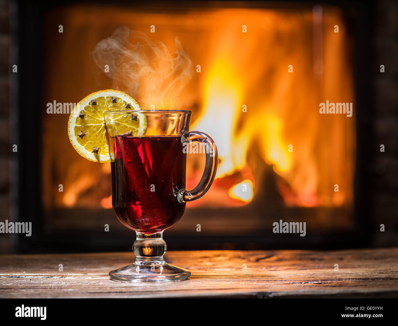 Vin brulé con fetta di arancia, chiodi di garofano e la stecca di cannella. Camino con fuoco caldo sullo sfondo. Foto Stock