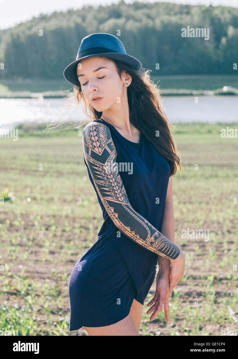 Hipster donna con manicotto di tatuaggio in piedi nel paesaggio rurale Foto Stock
