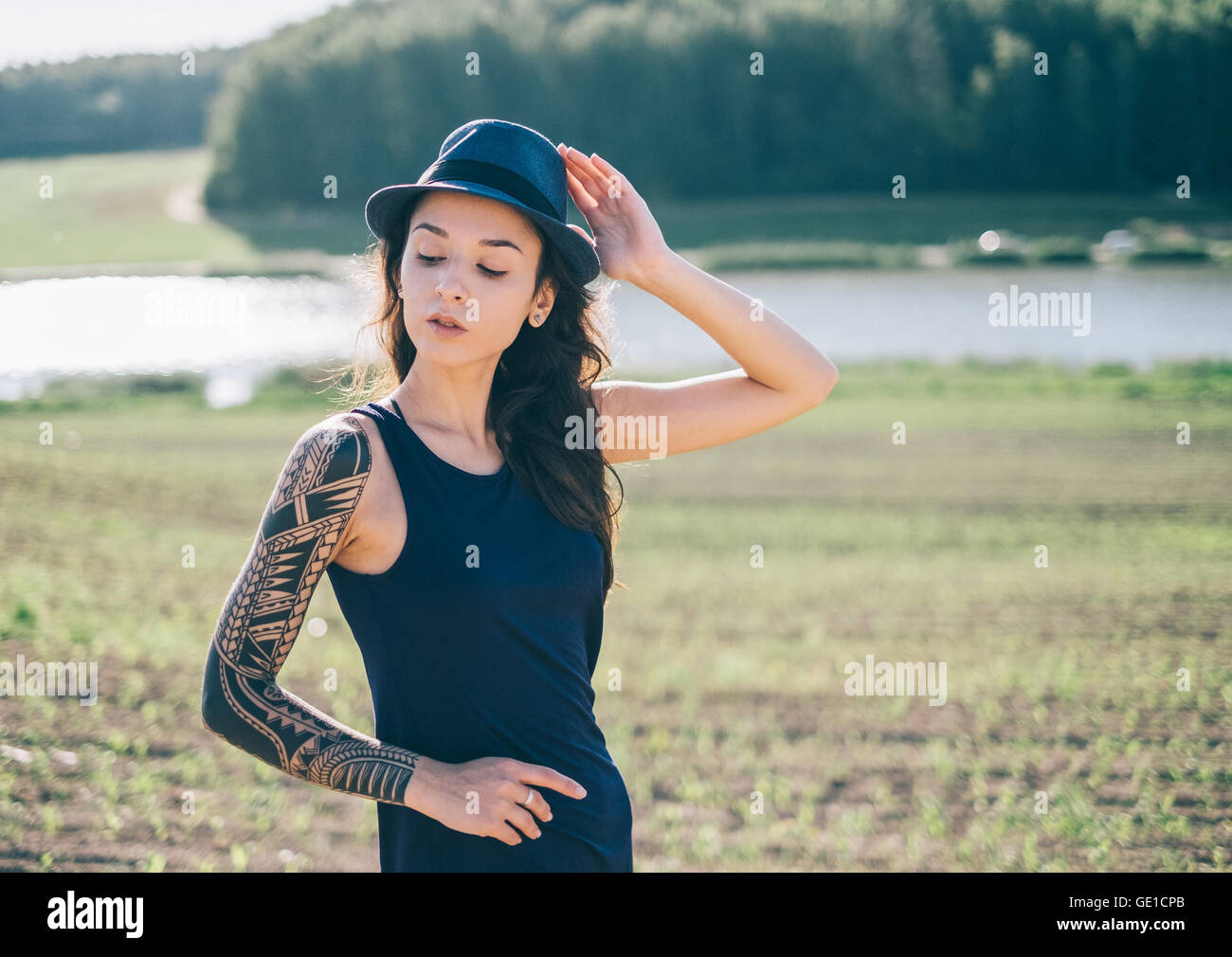 Hipster donna con manicotto di tatuaggio in piedi nel paesaggio rurale Foto Stock
