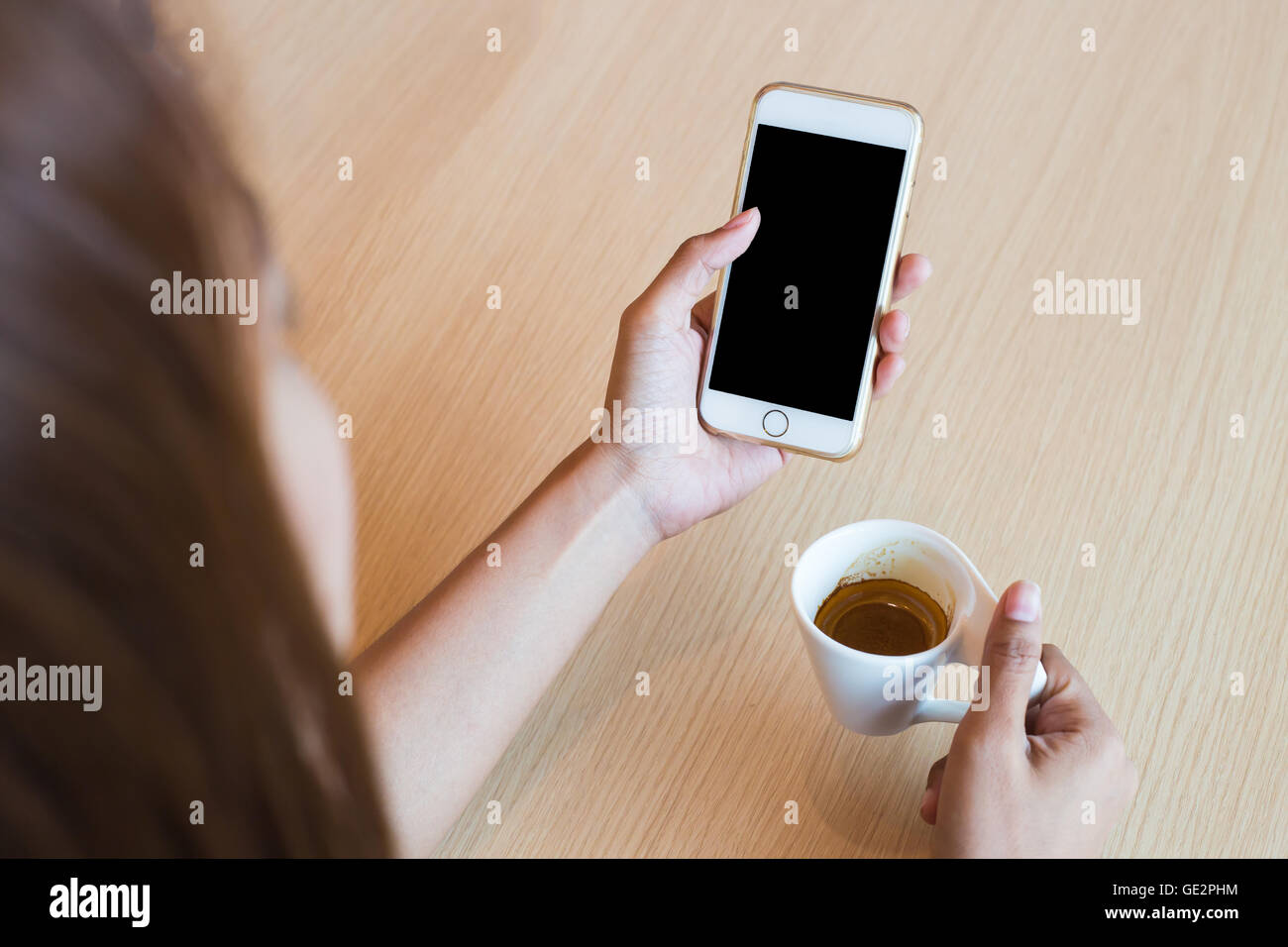 Donna che utilizza un touch screen di smartphone bianco sul tavolo di legno e la mano che regge il cappuccino aromatici, bianco tazza da caffè, chiudi Foto Stock