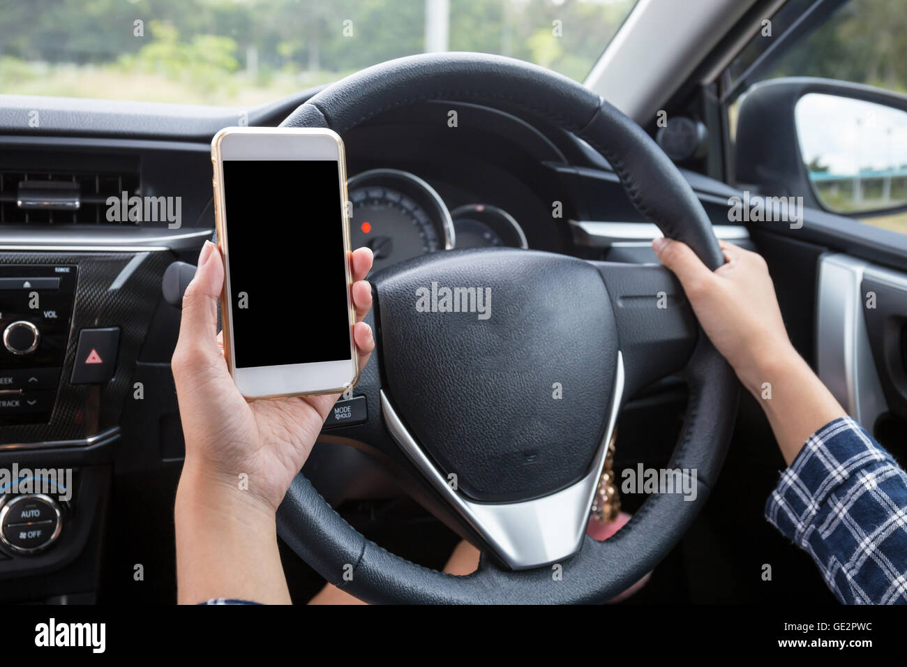Femmina giovane conducente utilizzando il touch screen smartphone e mano che tiene il volante in un'auto. Foto Stock