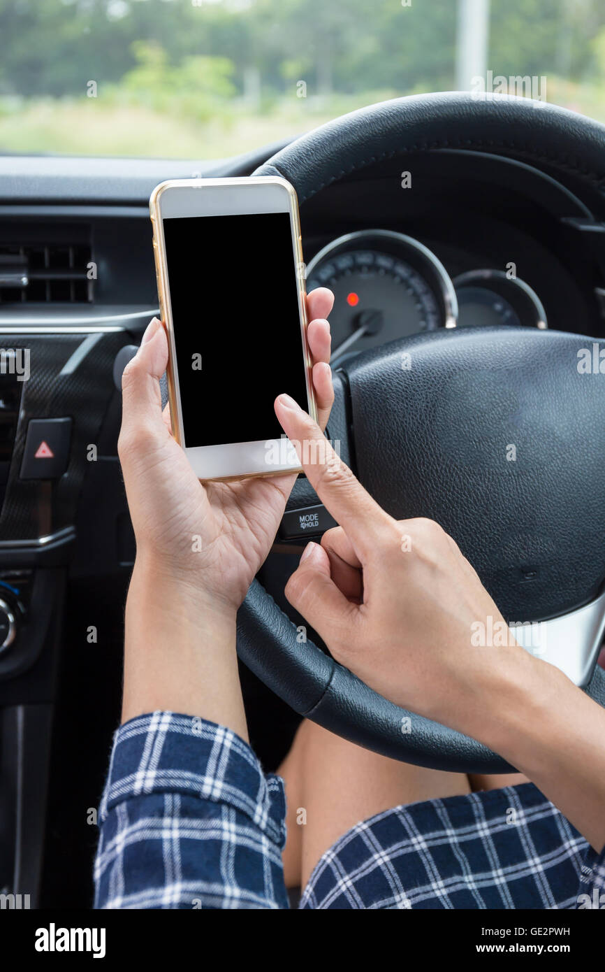 Femmina giovane conducente utilizzando il touch screen smartphone in un'auto. Foto Stock