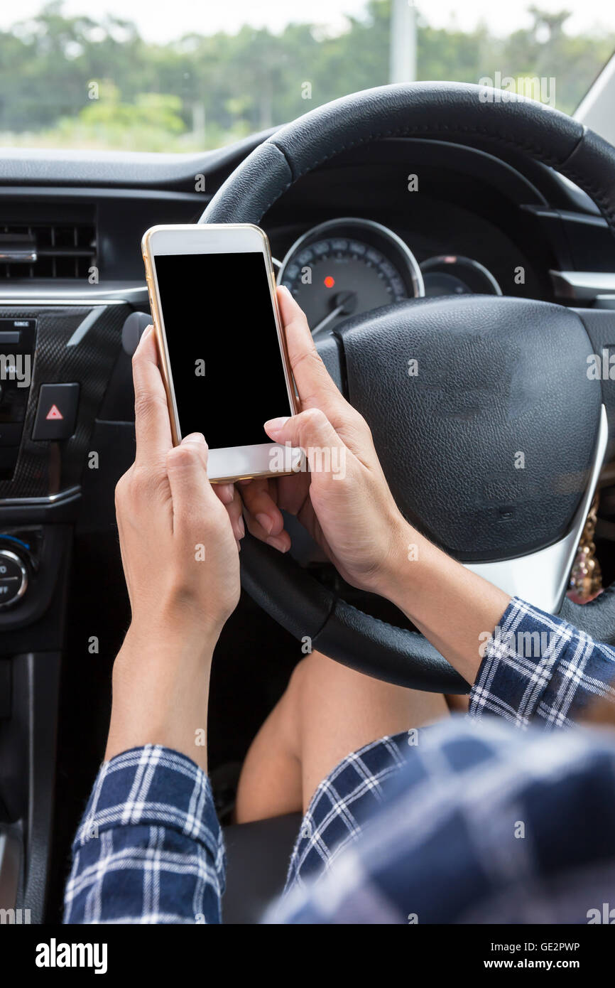 Femmina giovane conducente utilizzando il touch screen smartphone in un'auto. Foto Stock