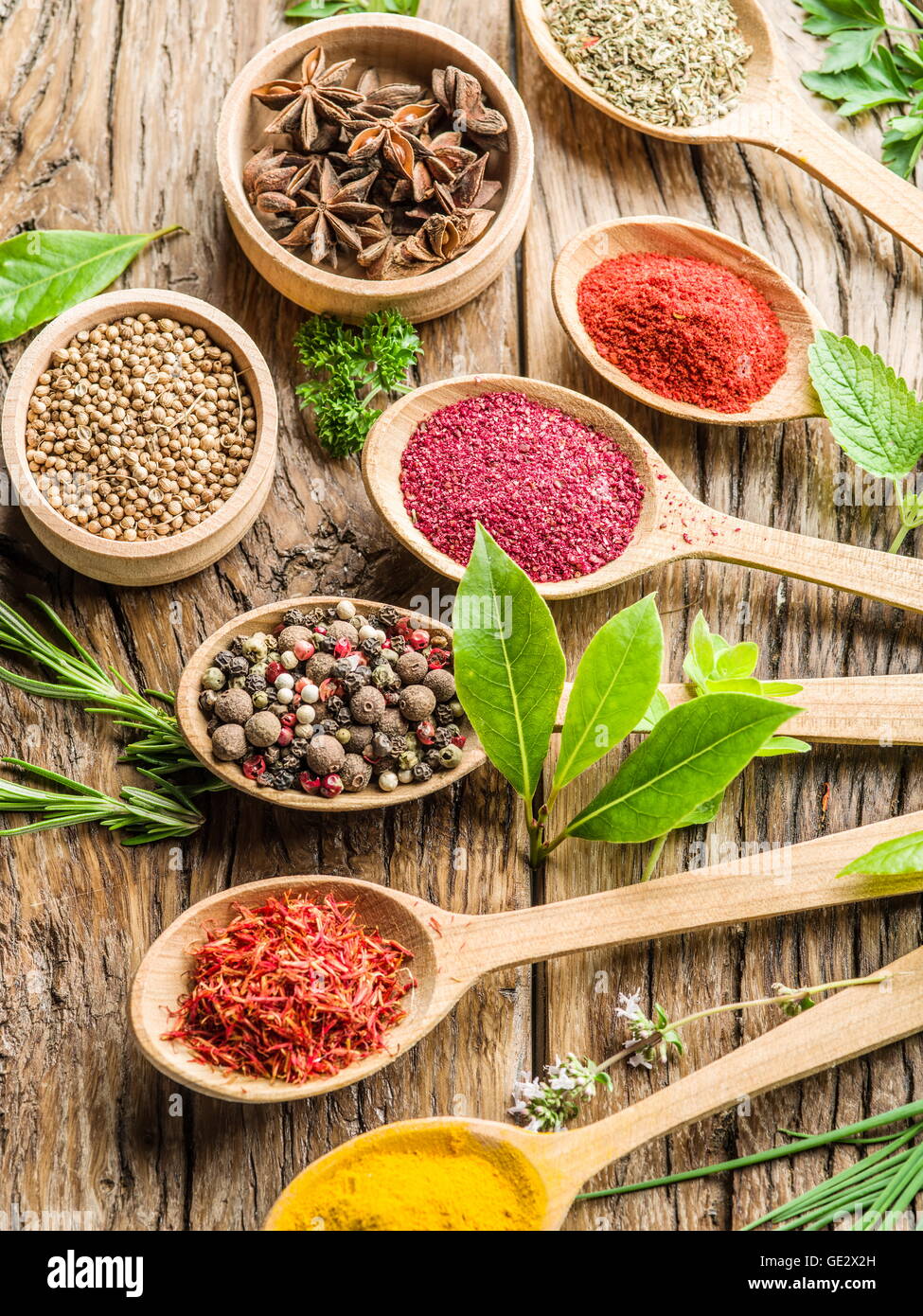 Assortimento di spezie colorate in i cucchiai di legno e le erbe sul tavolo di legno. Foto Stock