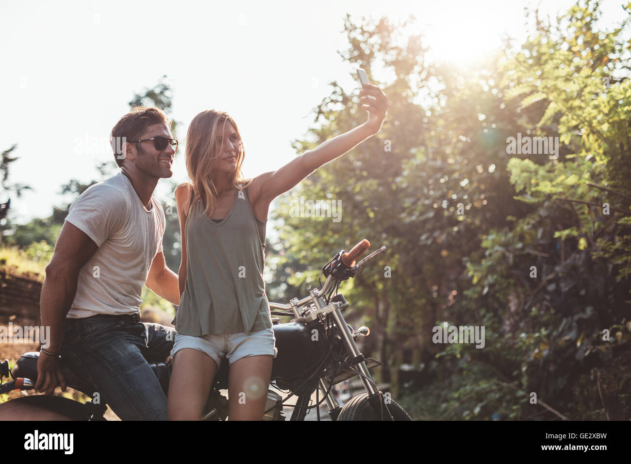 Inquadratura di un paio di prendere una selfie durante un viaggio con un motociclo. Coppia giovane divertirsi sul loro viaggio su strada. Foto Stock