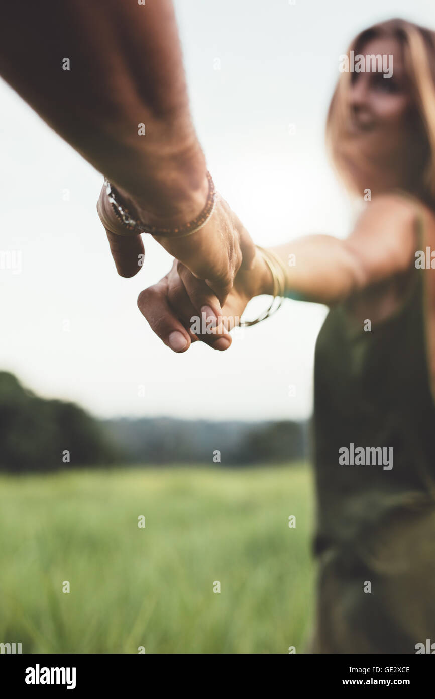 Immagine ravvicinata di man mano tesa della sua fidanzata nel campo d'erba. POV shot del giovane in natura. Foto Stock