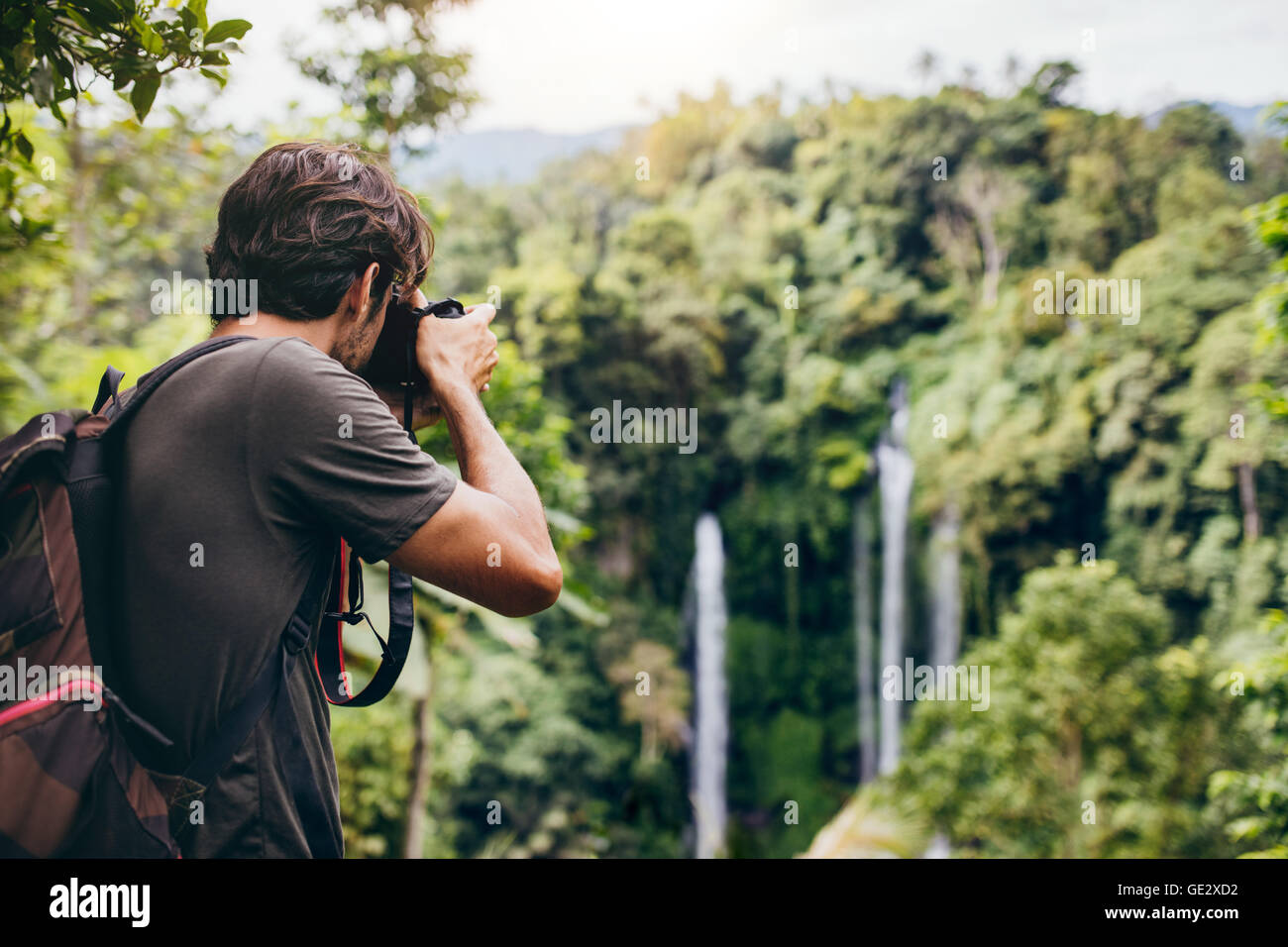 Uomo con zaino in piedi di fronte a cascata e di scattare una foto. Escursionista maschio fotografando un'acqua bella cadono nella foresta Foto Stock