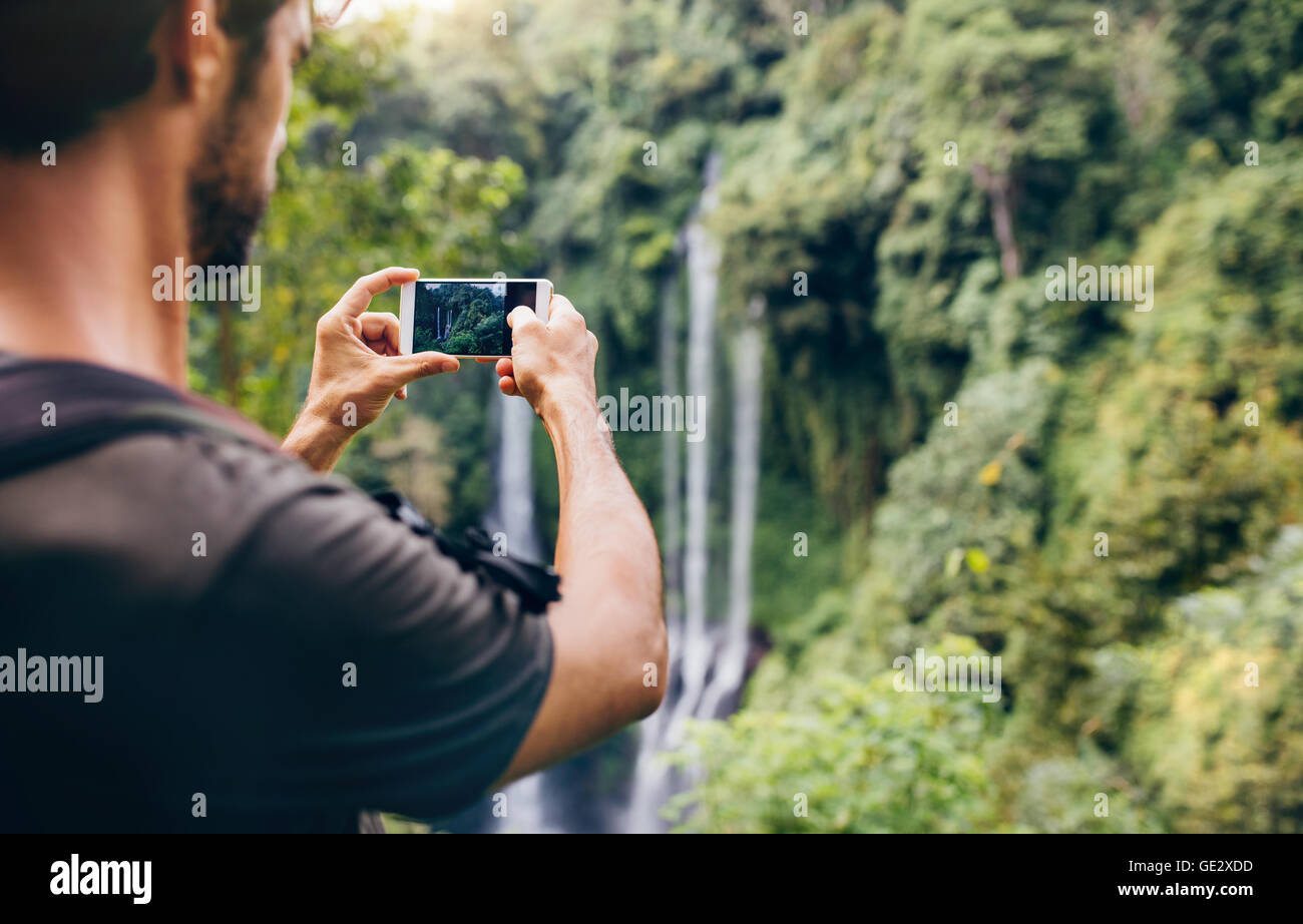 Close up di un uomo di scattare le foto della cascata con il suo cellulare. Escursionista maschio fotografando una caduta di acqua nella foresta. Foto Stock