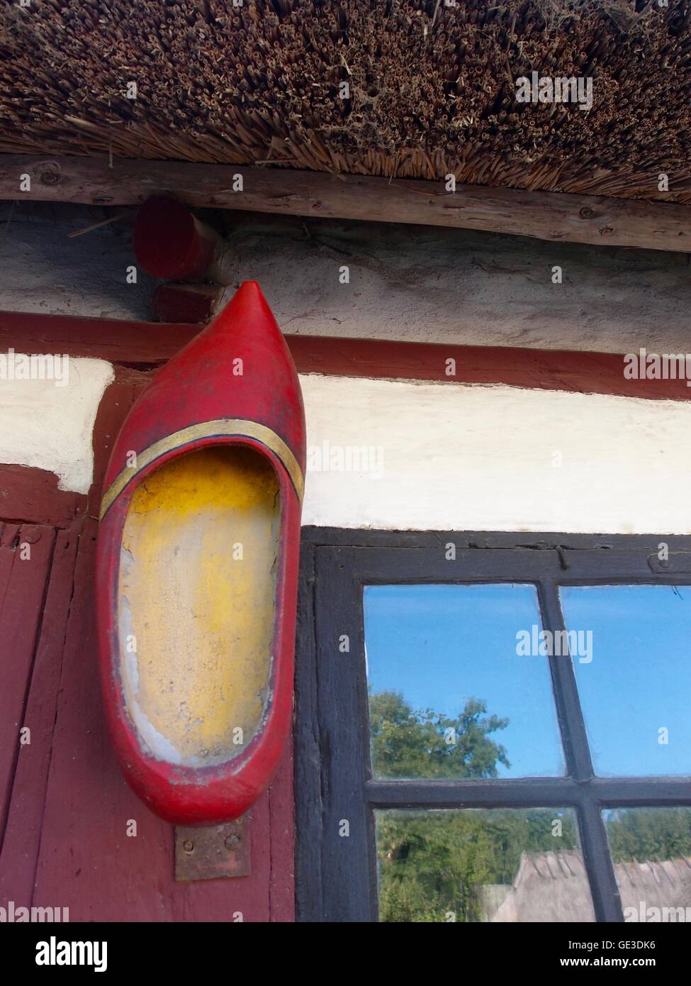 Grande, rosso, scarpe di legno appeso sul telaio della porta, sul vecchio secolo la casa con tetto di paglia. Foto Stock