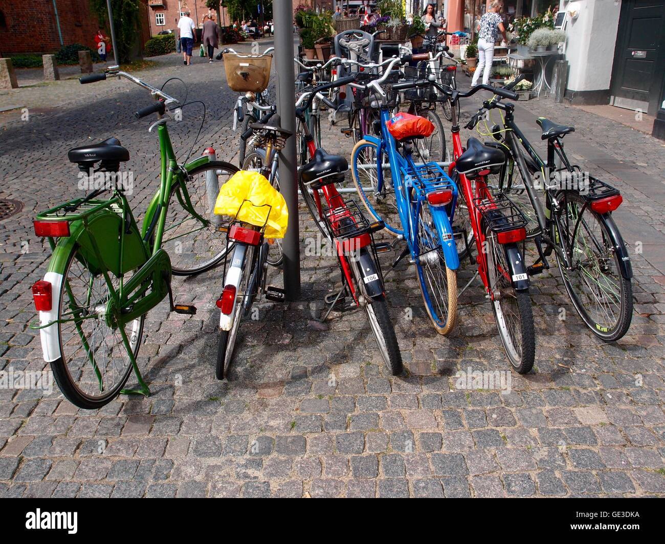 Supporto per bicicletta con colorati biciclette parcheggiate, su una strada di ciottoli. Foto Stock