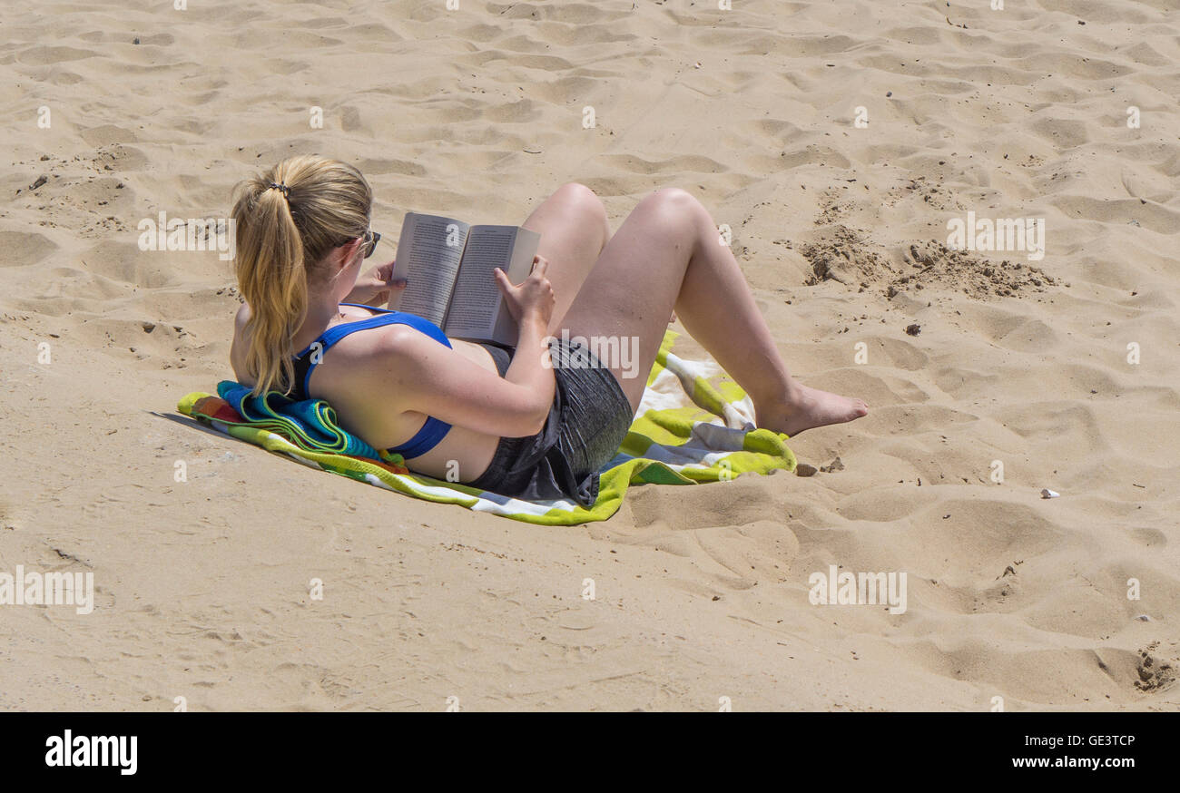 Una giovane donna si rilassa sotto il sole la lettura di un libro sulla spiaggia a Bournemouth, Regno Unito Foto Stock