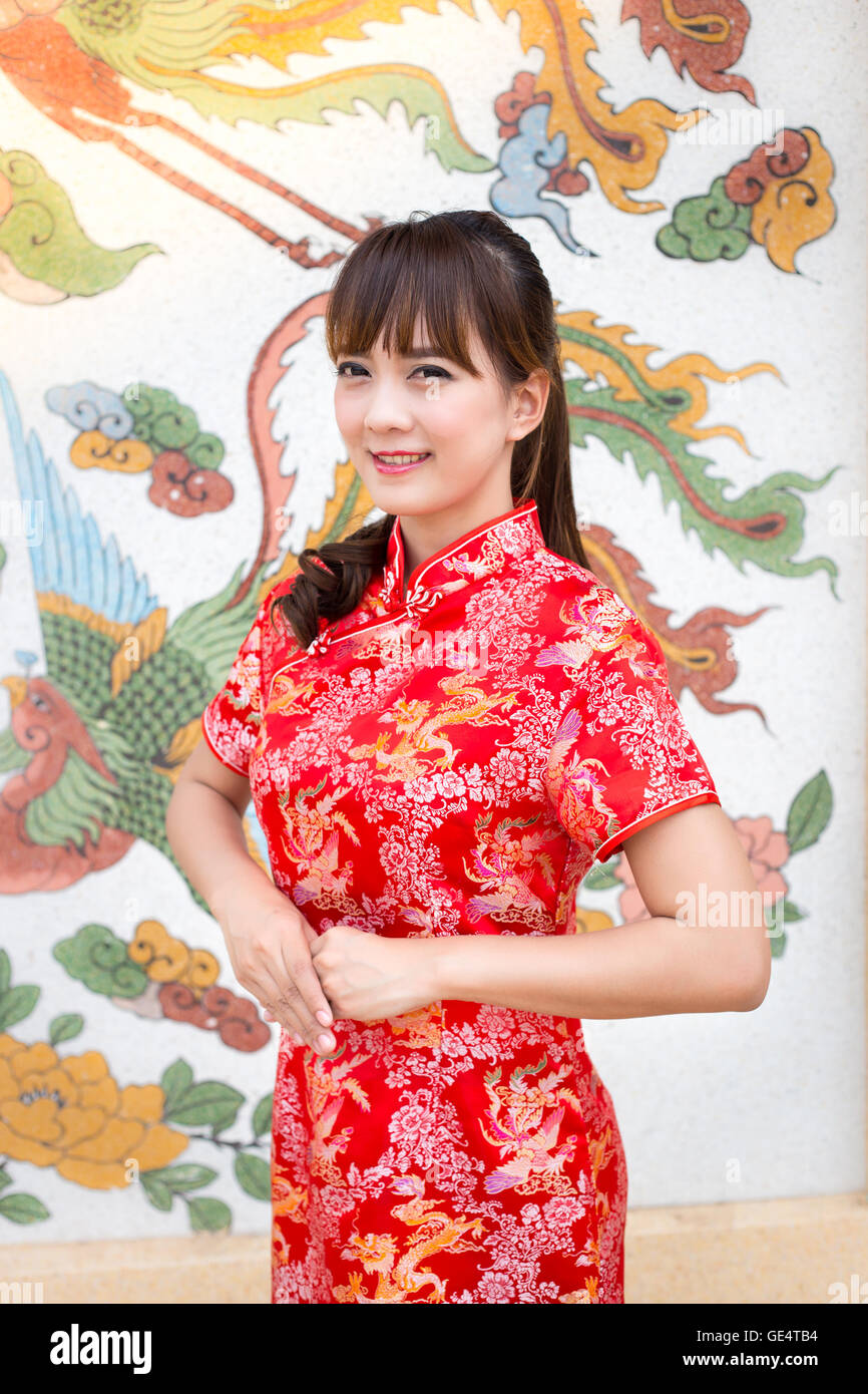 Felice anno nuovo cinese. Carino donna asiatica con gesto di congratulazione isolato sul rosso modello cinese sfondo tradizionale Foto Stock