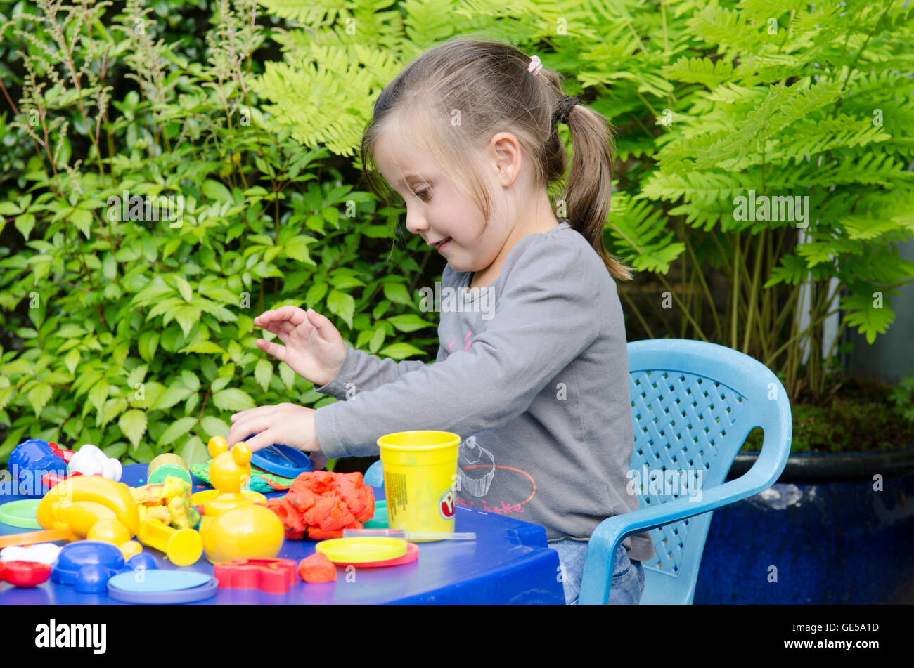 Bimba di tre anni gioca con la modellazione Play-Doh putty. Regno Unito. Fuori in giardino. Foto Stock