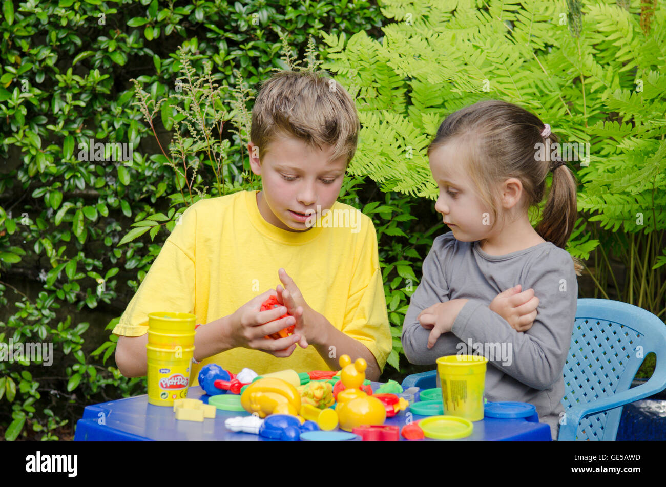 Bimba di tre anni e dieci-anno-vecchio ragazzo, fratello e sorella, giocando con la modellazione Play-Doh putty. Regno Unito. Fuori in giardino. Foto Stock