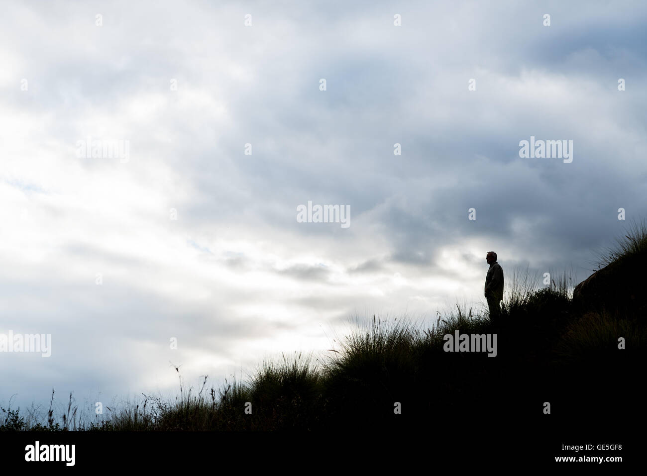 Uomo in silhouette sulla collina con sfondo con cielo nuvoloso Foto Stock