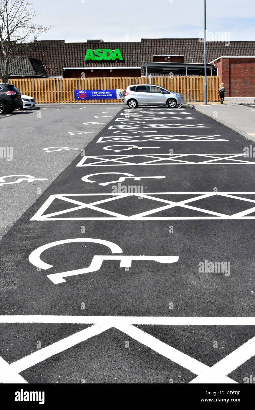 Disabili e disabilità gli utenti supermercato Asda car park una persona su sedia a rotelle parcheggiata nella baia di designati tutti gli spazi adiacenti vuote pittogramma mostra icone Foto Stock
