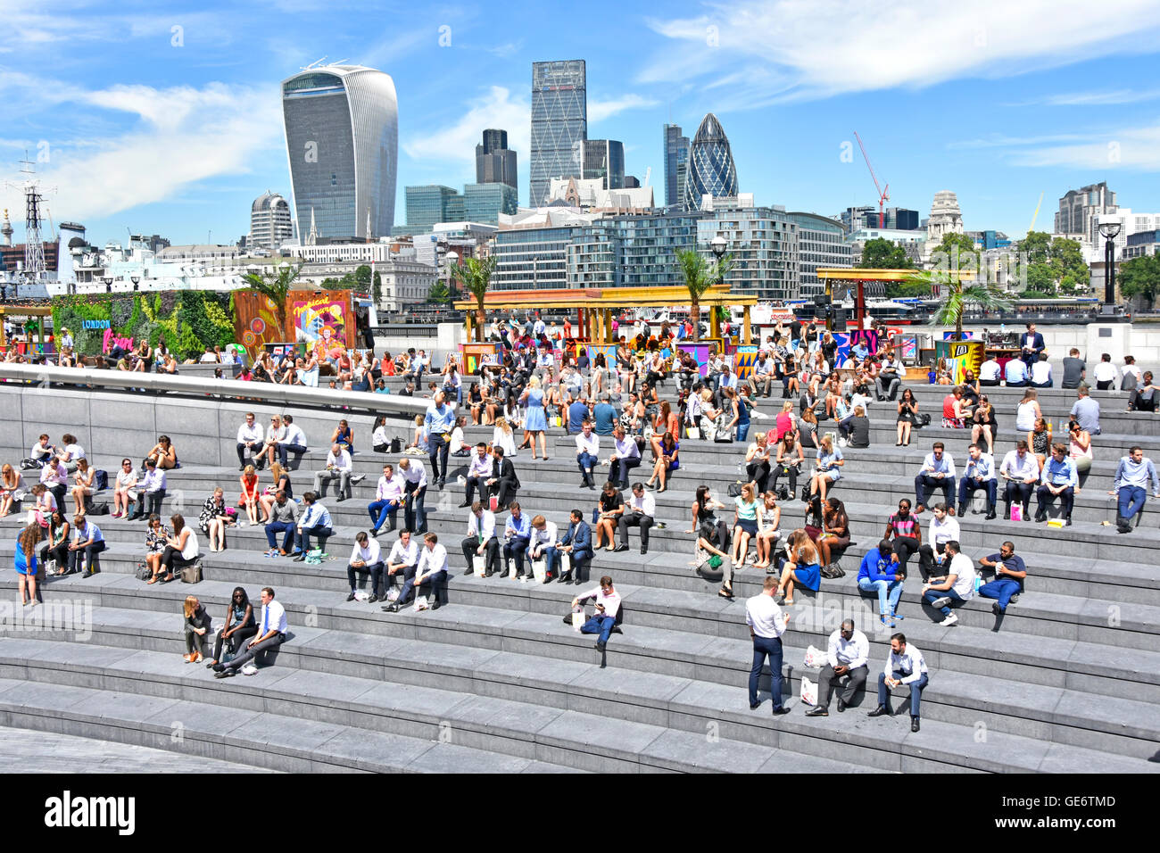 Ufficio di Southwark lavoratori tenuto caldo del soleggiato pausa pranzo al più Londra Scoop riverside anfiteatro con City Of London skyline al di là dell'Inghilterra, Regno Unito Foto Stock