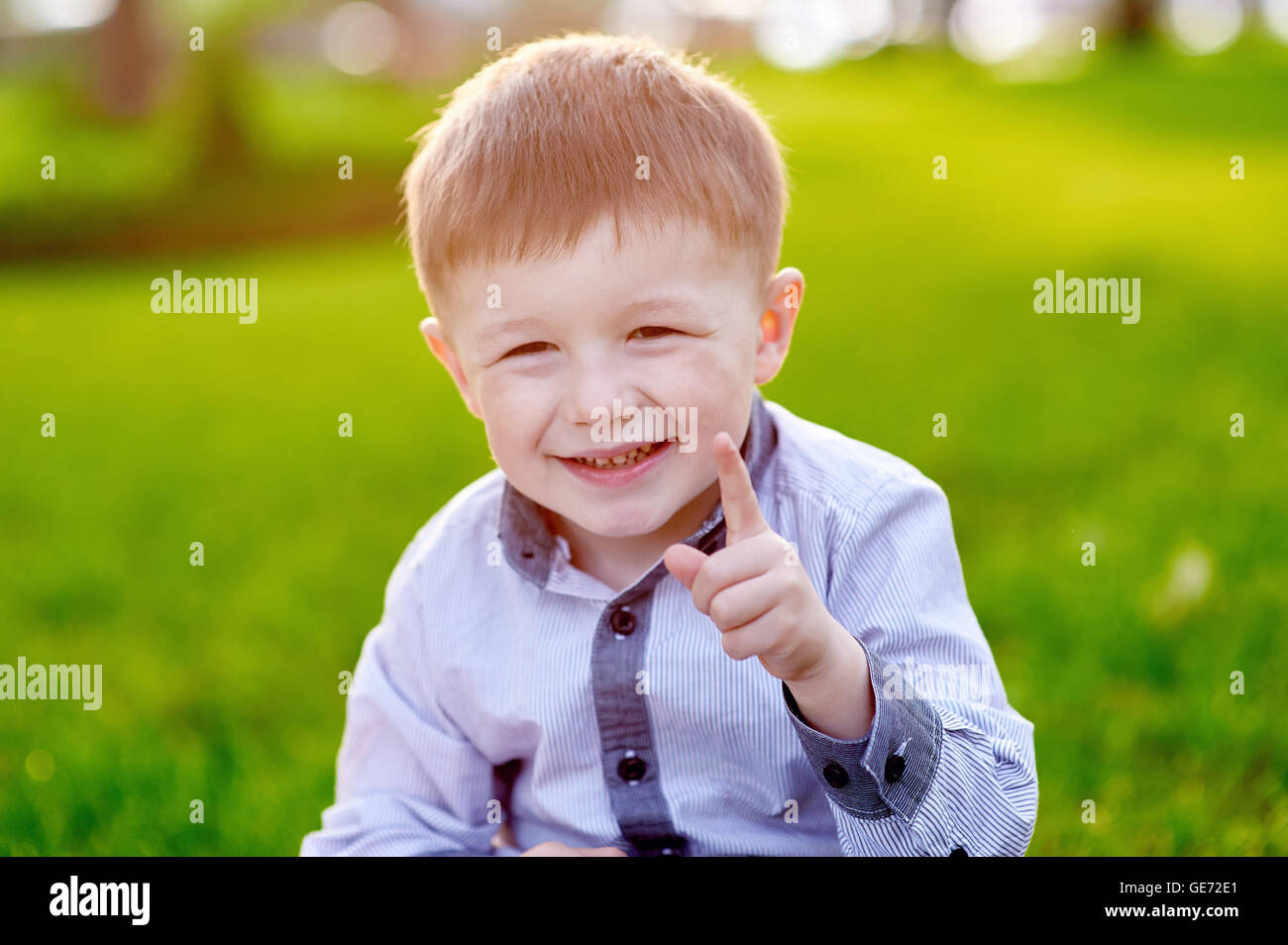 Allegro piccolo ragazzo seduto sull'erba nel parco Foto Stock