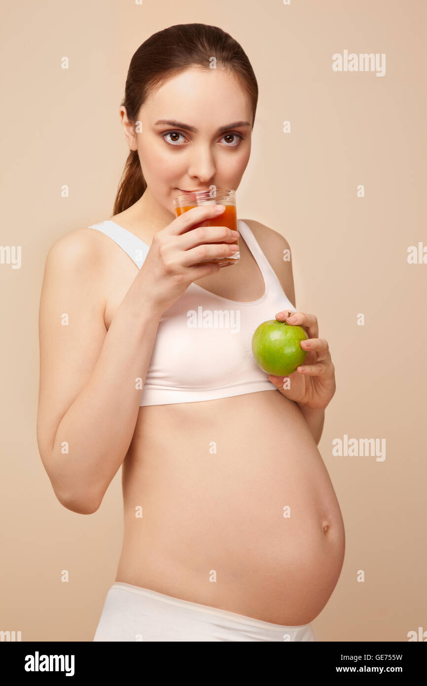 Bella donna incinta tenendo un bicchiere di succo di frutta e mela verde Foto Stock