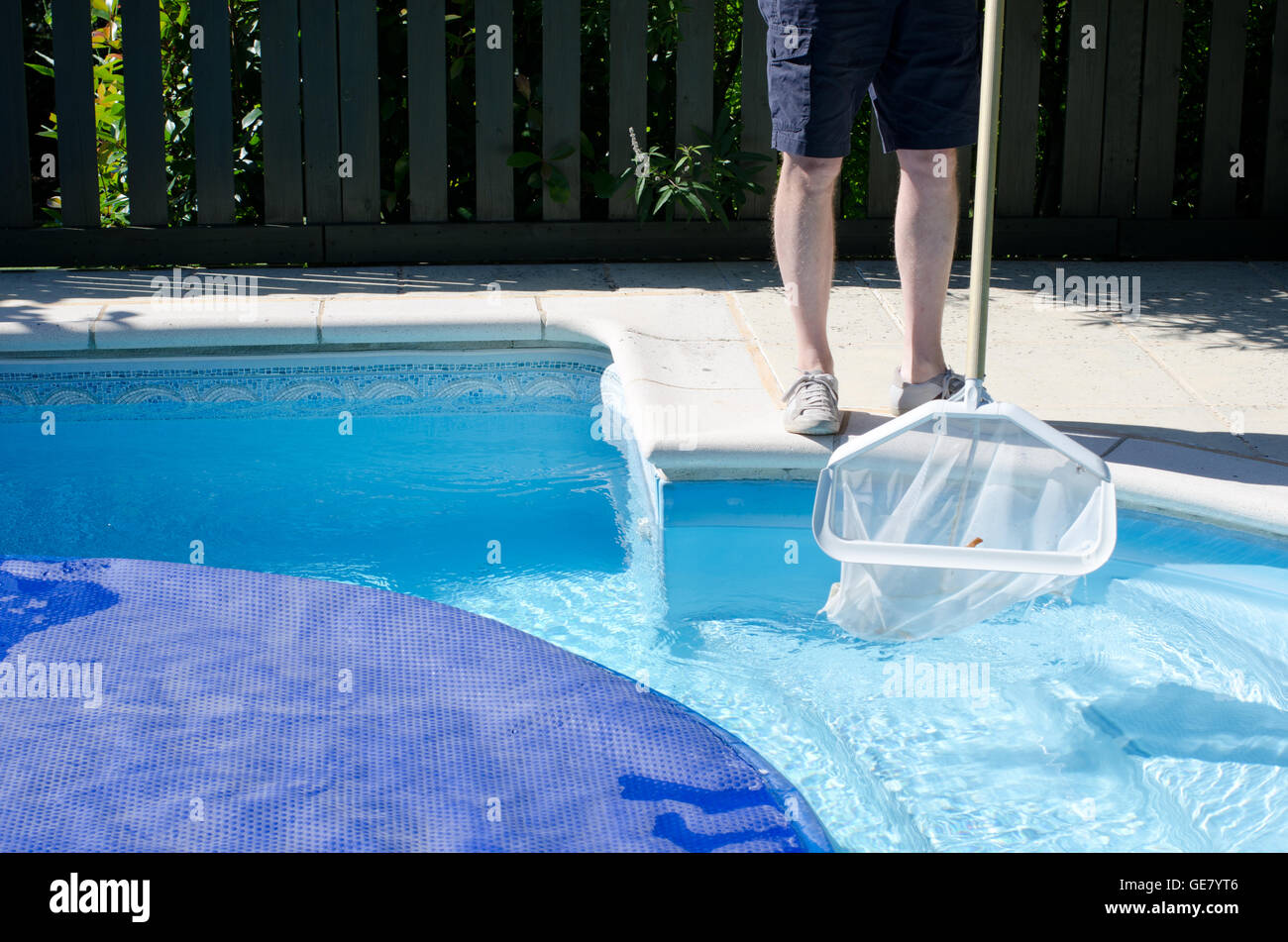 Un uomo con una pulizia netto l'ultima parte della piscina prima che il coperchio si accende Foto Stock