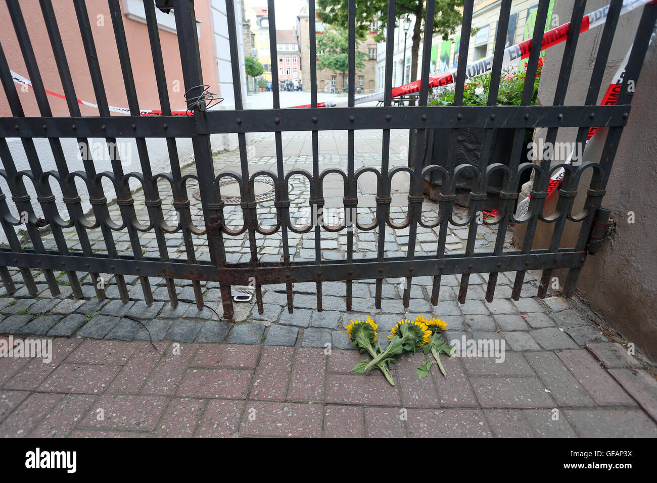 Ansbach, Germania. Xxv Luglio, 2016. Girasoli giacciono da un cancello chiuso dietro il nastro di polizia vicino la scena del crimine nella città vecchia di Ansbach, Germania, 25 luglio 2016. 15 persone sono rimaste ferite in un presunto di islamisti-attacco motivato il 24 luglio 2016. Il sospettato colpevole, un 27-anno-vecchio rifugiato dalla Siria, è stato ucciso in un attacco. Foto: KARL-JOSEF HILDENBRAND/dpa/Alamy Live News Foto Stock