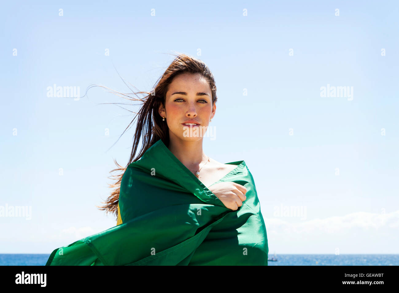 Bruna giovane donna che gioca con la bandiera brasiliana in spiaggia Foto Stock