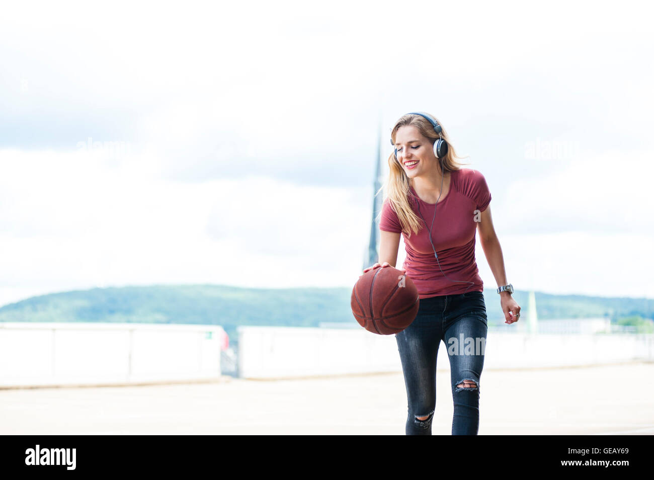 Sorridente giovane donna con le cuffie a giocare con basket sulla terrazza sul tetto Foto Stock