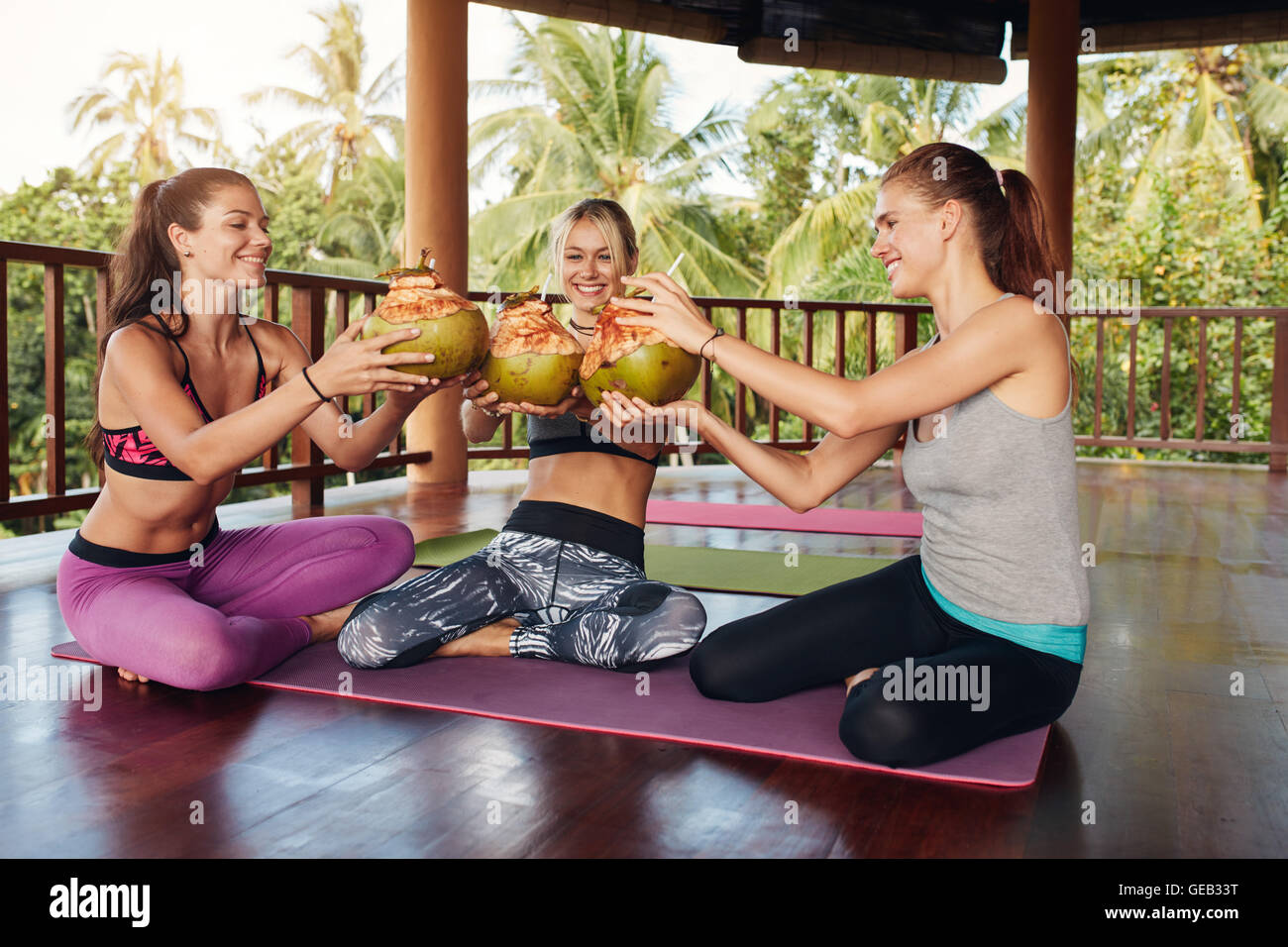 Colpo di un gruppo di giovani amici di sesso femminile tostare le noci di cocco verde a lezione di yoga. Gruppo di idoneità femmina presentando un succo di cocco durante Foto Stock