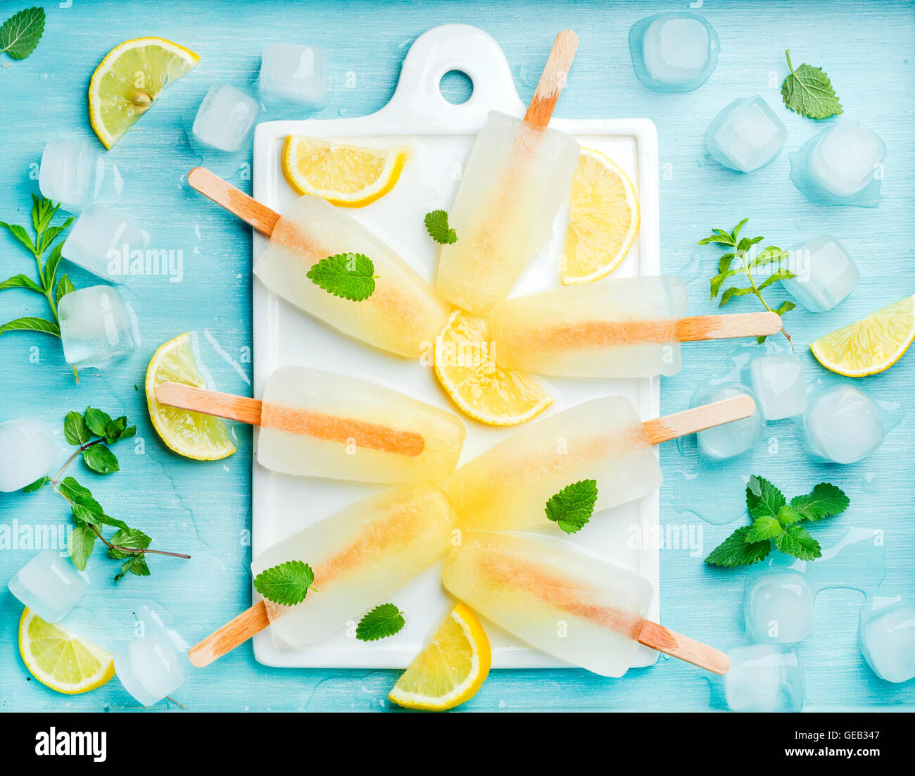La limonata popsicles con le fette di limone e foglie di menta fresca e cubetti di ghiaccio su bianco scheda di ceramica Foto Stock