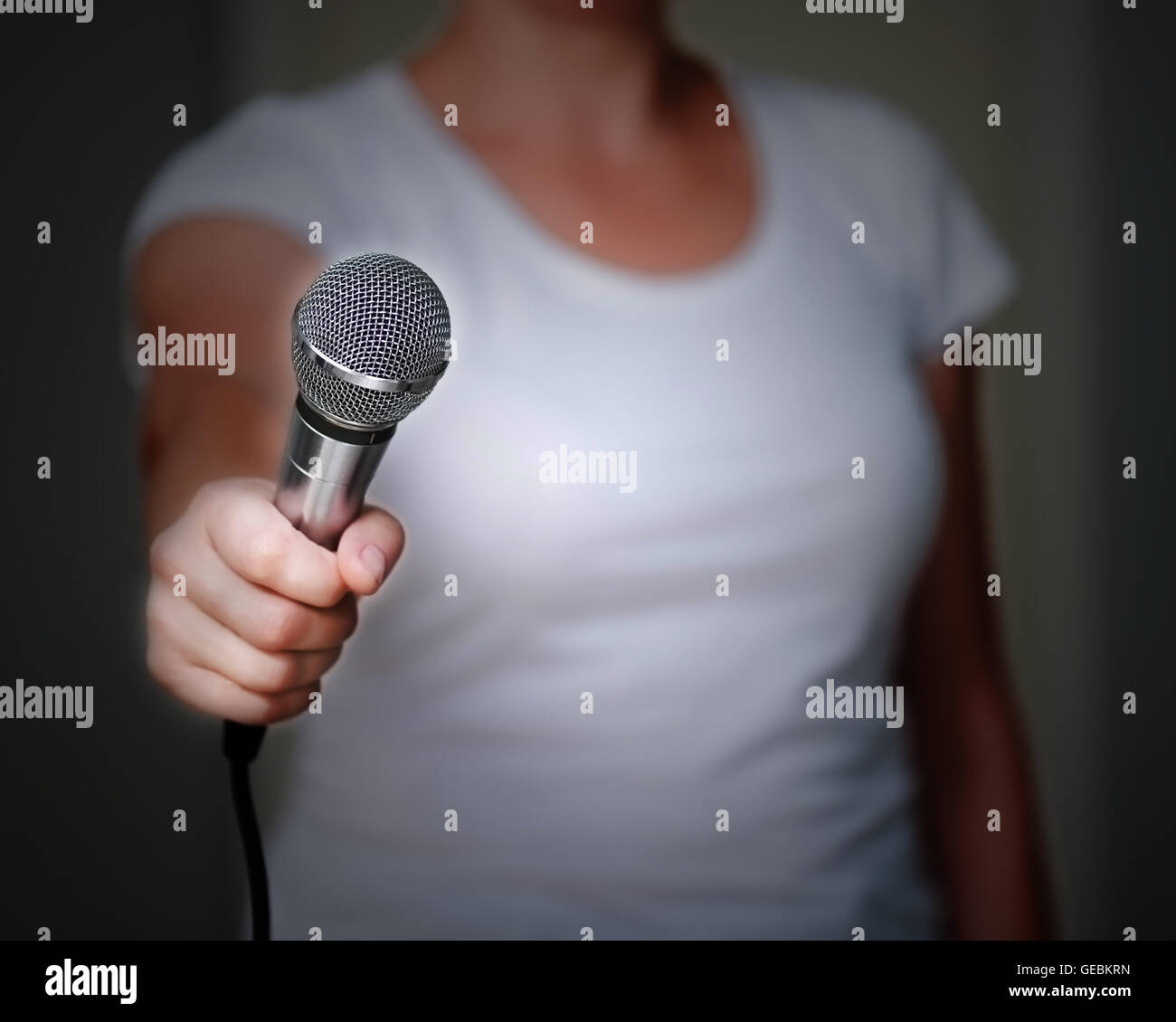 Close up della donna in maglia bianca, che offre a qualcuno di darle un'intervista. Tenendo il microfono in mano. Foto Stock