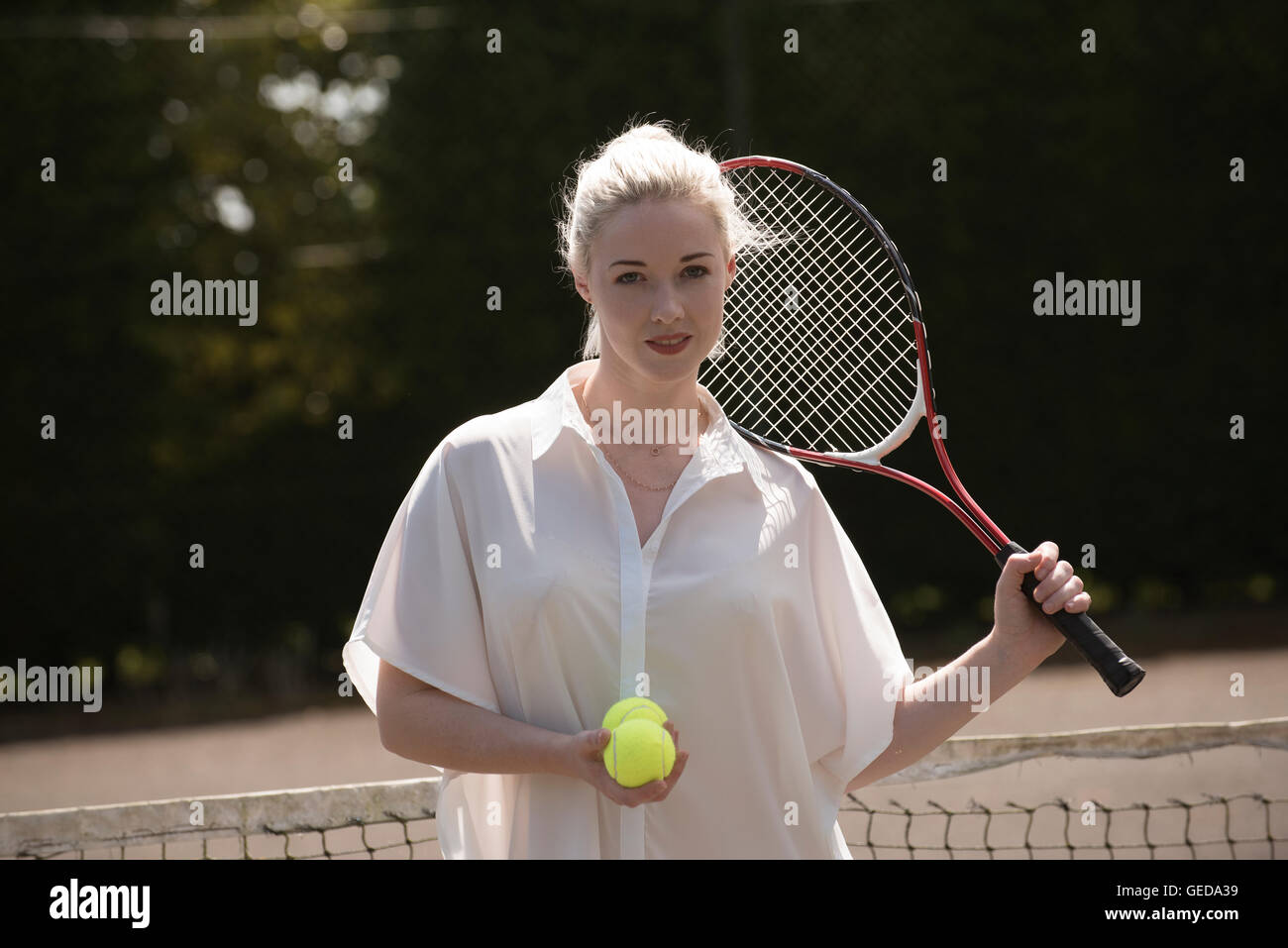 Ritratto di un giovane giocatore di tennis. Una femmina giovane giocatore di tennis con capelli biondi tenendo un racchette e palle da tennis Foto Stock