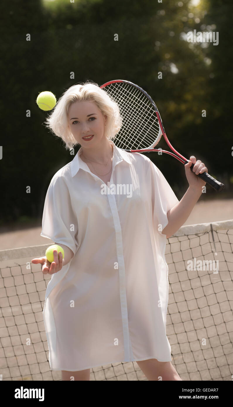 Ritratto di un giovane giocatore di tennis. Una femmina giovane giocatore di tennis con capelli biondi tenendo un racchette e palle da tennis Foto Stock