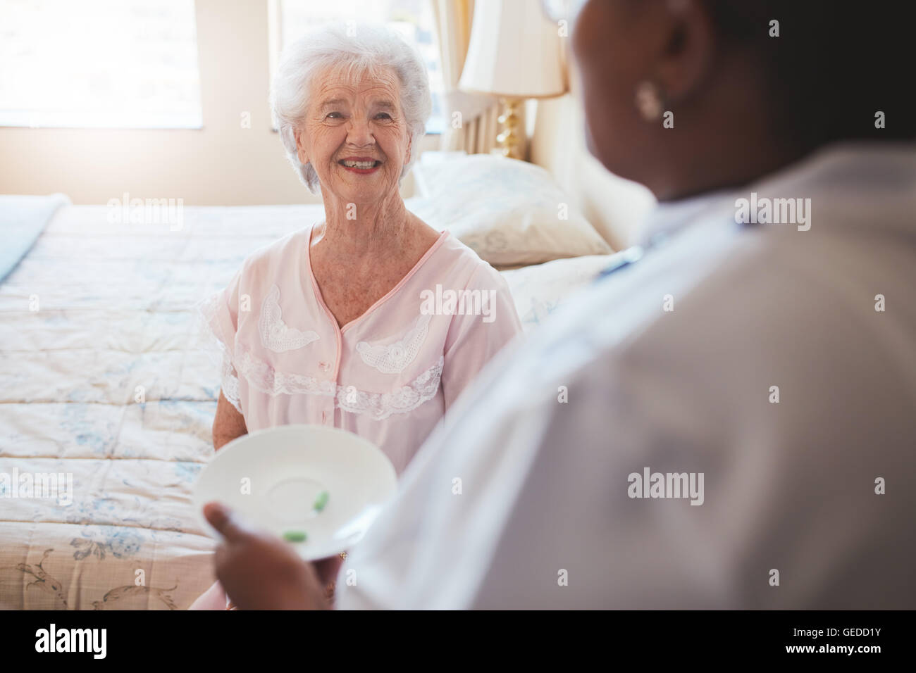 Piscina colpo di senior donna seduta sul letto e home care nurse dando farmaco. Anziani caucasica donna sorridente. Foto Stock