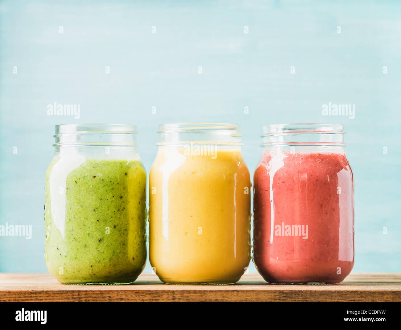 Mescolate freschi frullati di frutta di vari colori e sapori in vasetti di vetro. Verde, giallo, rosso. Foto Stock