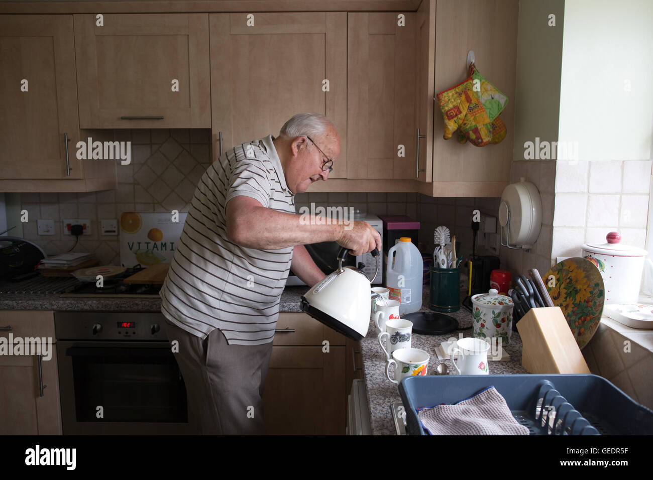 La vecchiaia pensionato rendendo tazze di tè per i visitatori nella sua cucina a casa in Inghilterra, Regno Unito Foto Stock