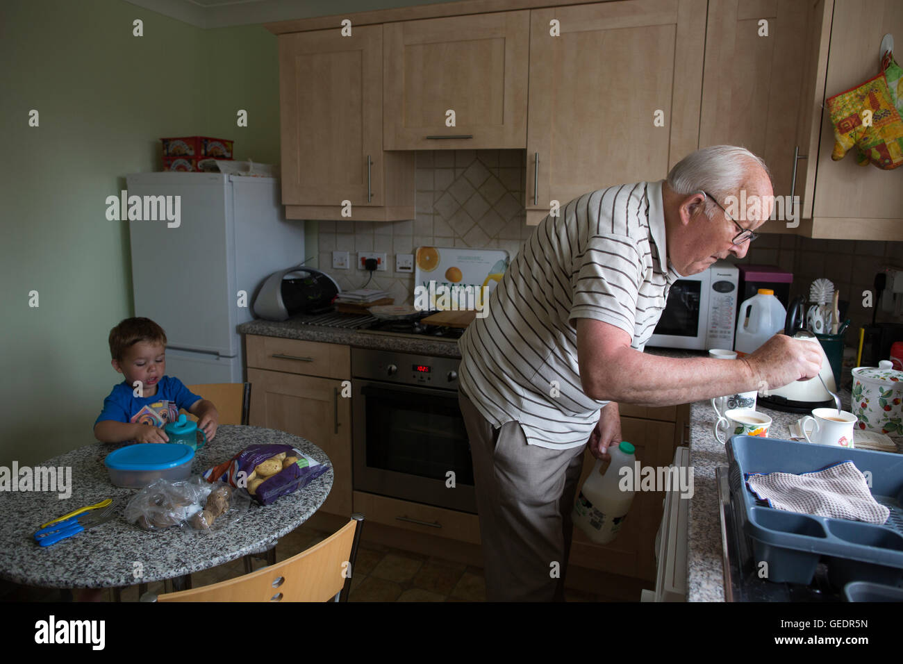 La vecchiaia titolare di pensione o di rendita (83 anni) in cucina con il suo nipote (di età compresa tra i 2) in Inghilterra, Regno Unito Foto Stock