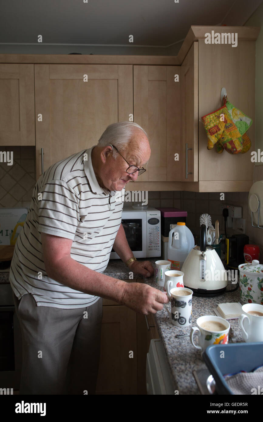 La vecchiaia pensionato rendendo tazze di tè per i visitatori nella sua cucina a casa in Inghilterra, Regno Unito Foto Stock