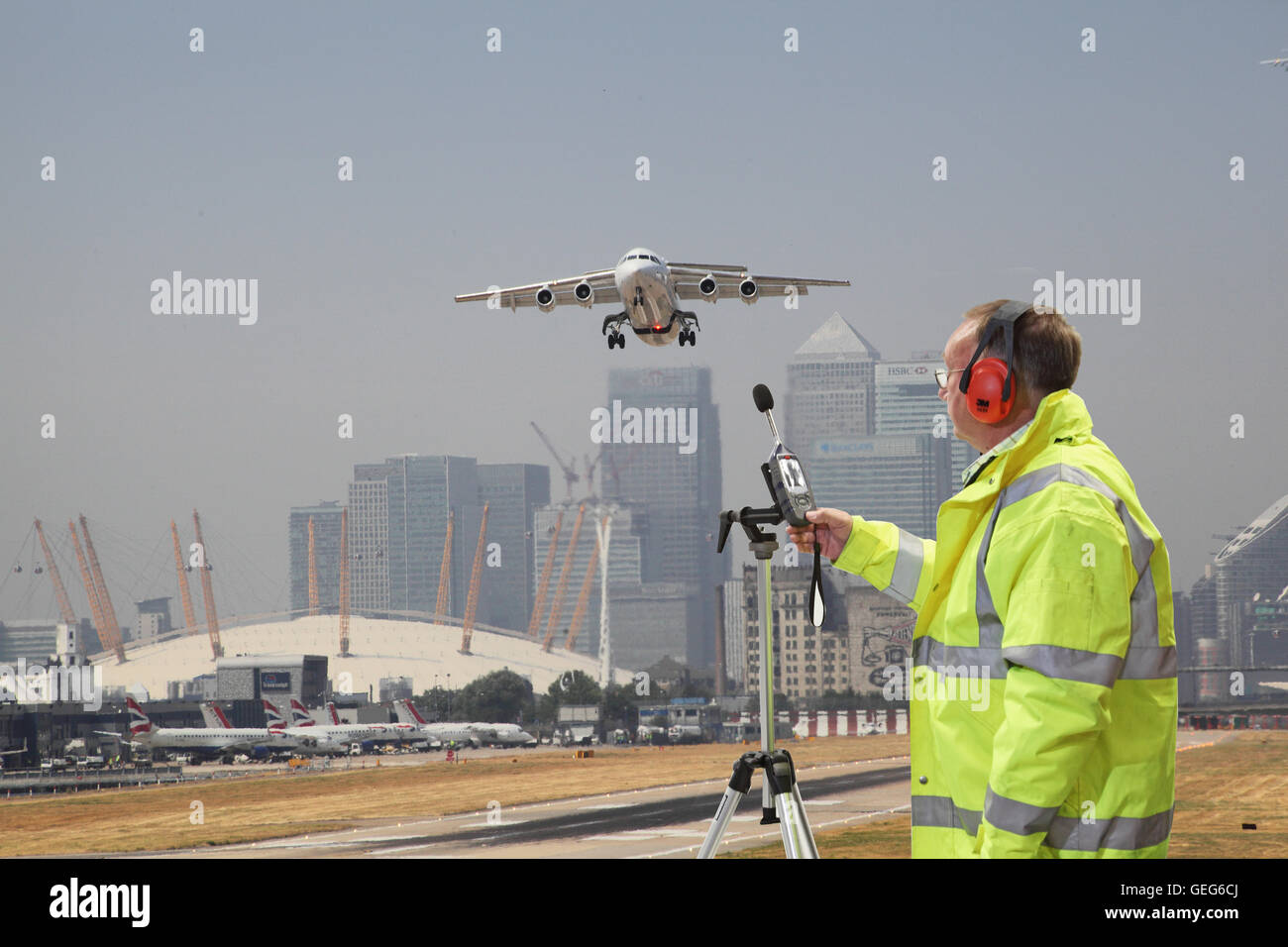 Un ingegnere ambientale controlla i livelli di rumore all'Aeroporto di London City come piano prende il largo. Canary Wharf in background. Foto Stock
