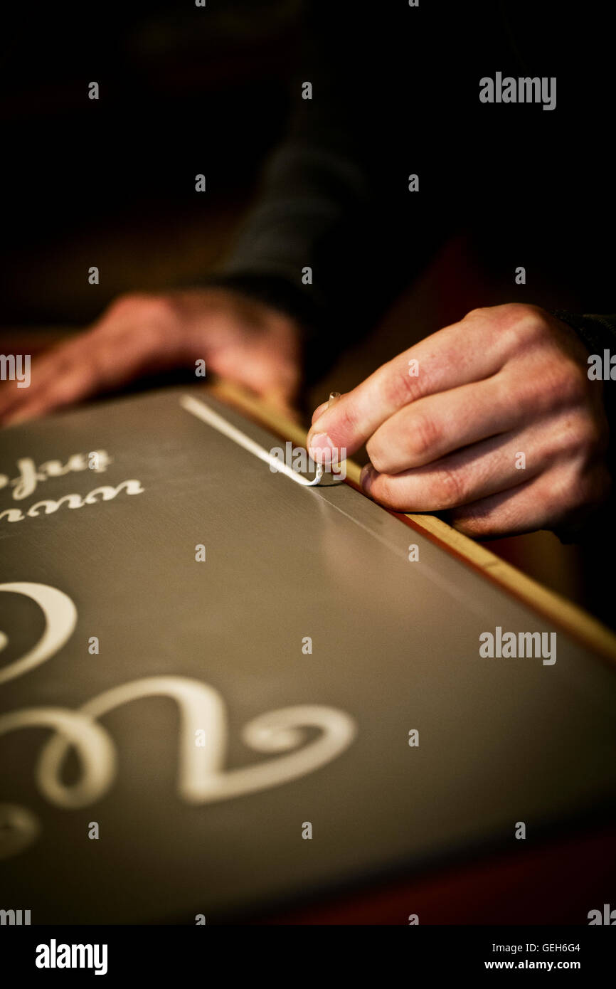 Un segno scrittore lavora con un carico verniciatura a pennello una linea freehand sul bordo di un segno. Foto Stock