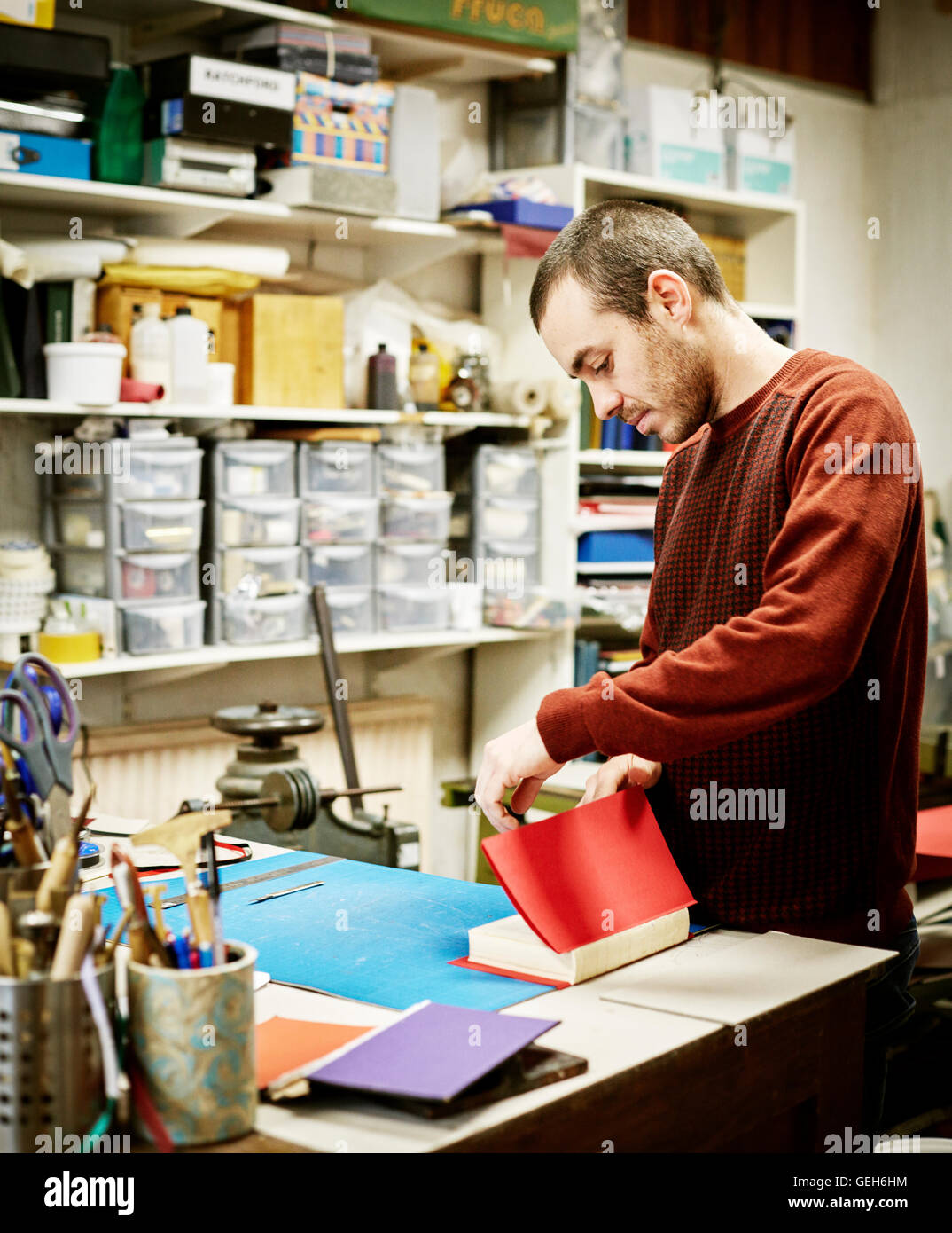 Un uomo che lavora in una rilegatura libro workshop, creazione di un coperchio rosso appena cucito pagine. Foto Stock
