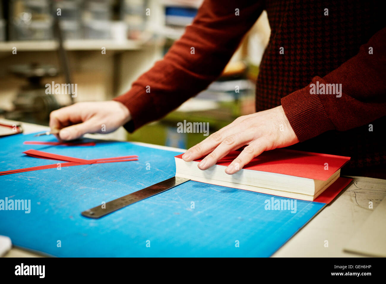 Uomo al lavoro su un banco, per misurare e tagliare il materiale per il recupero di un libro, in un workshop di rilegatura di libri. Foto Stock