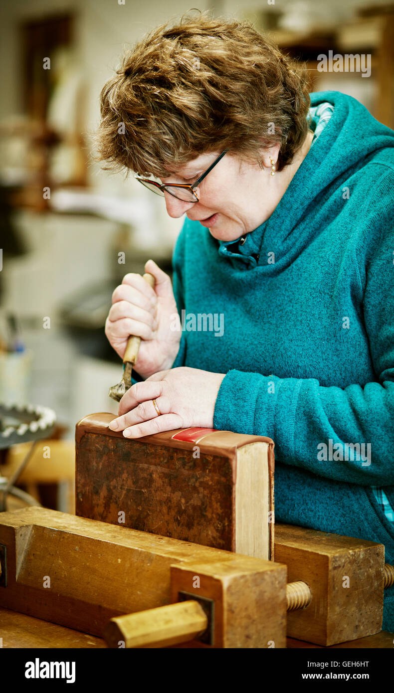 Una donna che lavorano sul dorso di un libro rilegato con un attrezzo a mano. Foto Stock