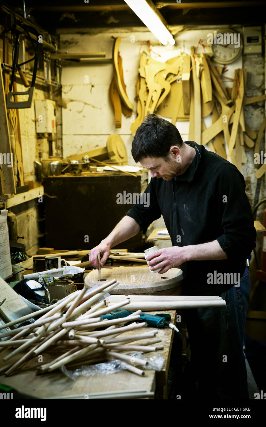 Un uomo che lavora in un produttore di mobili della bottega. Gambe di sedie sul banco di lavoro. Foto Stock