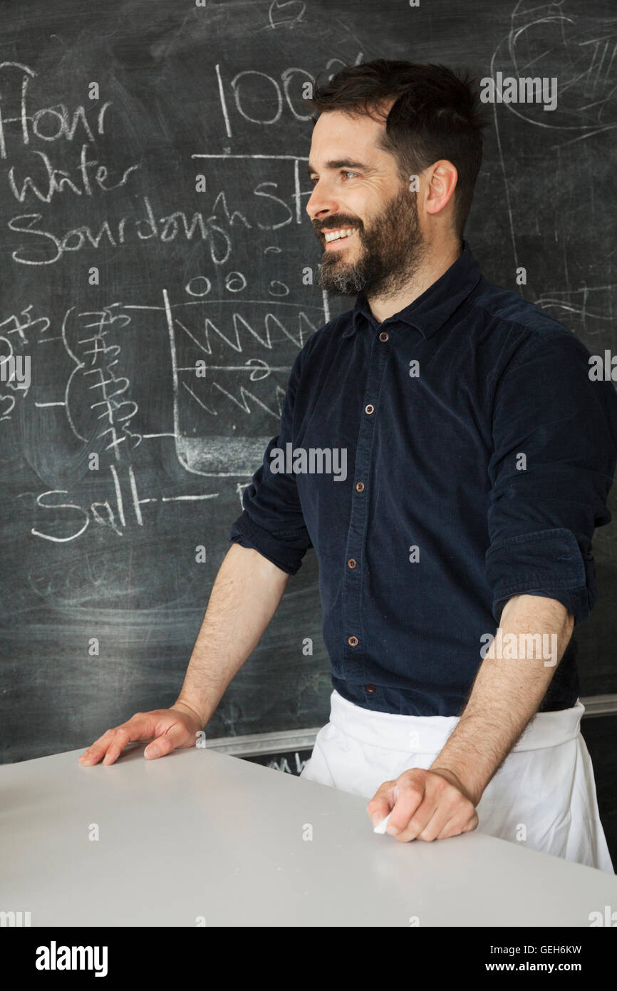 Baker in piedi di fronte a una lavagna con una ricetta per il pane scritto su di esso. Foto Stock