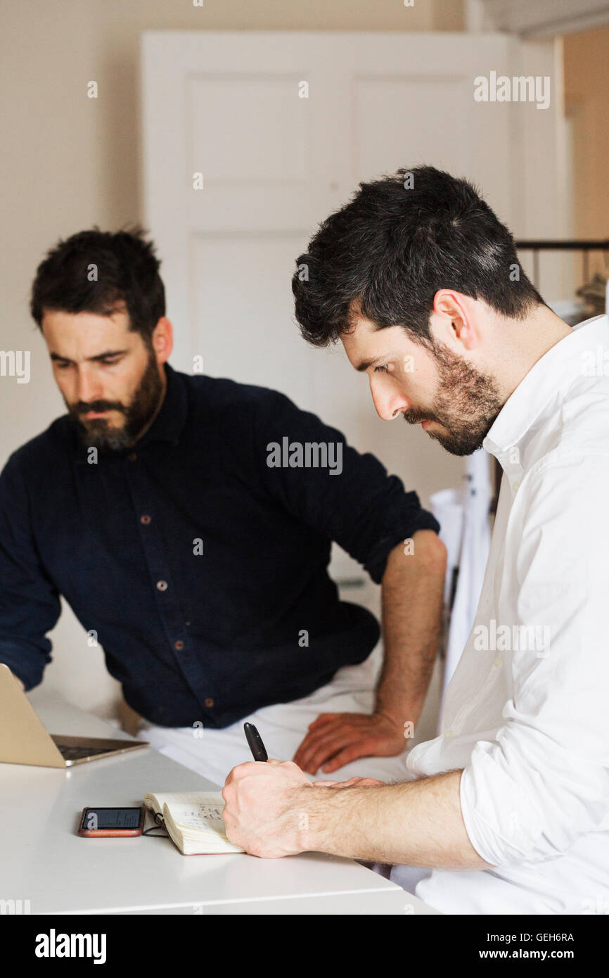 Due uomo barbuto in una panetteria, la scrittura di un notebook e di lavorare su un computer portatile. Foto Stock