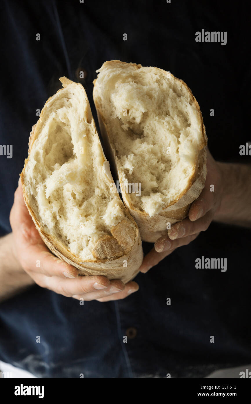 Close up di un fornaio tenendo un fresco bianco cotto il pane strappato a metà. Foto Stock