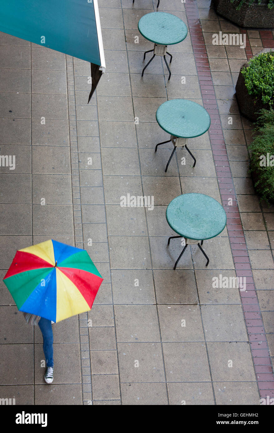 Svuotare il caffe di tabelle in un giorno di pioggia. Qualcuno con ombrello passeggiando a. Foto Stock